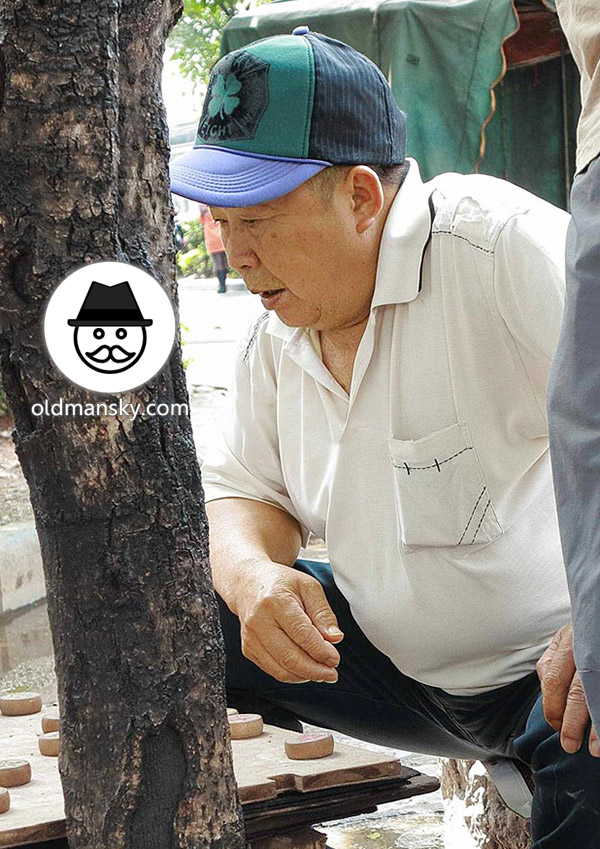 Old daddy wore white polo shirt was playing Chinese chess in the park