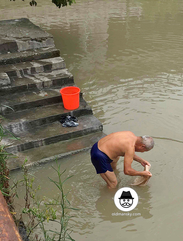 White hair old man wore a brown underwear was washing his head by the river